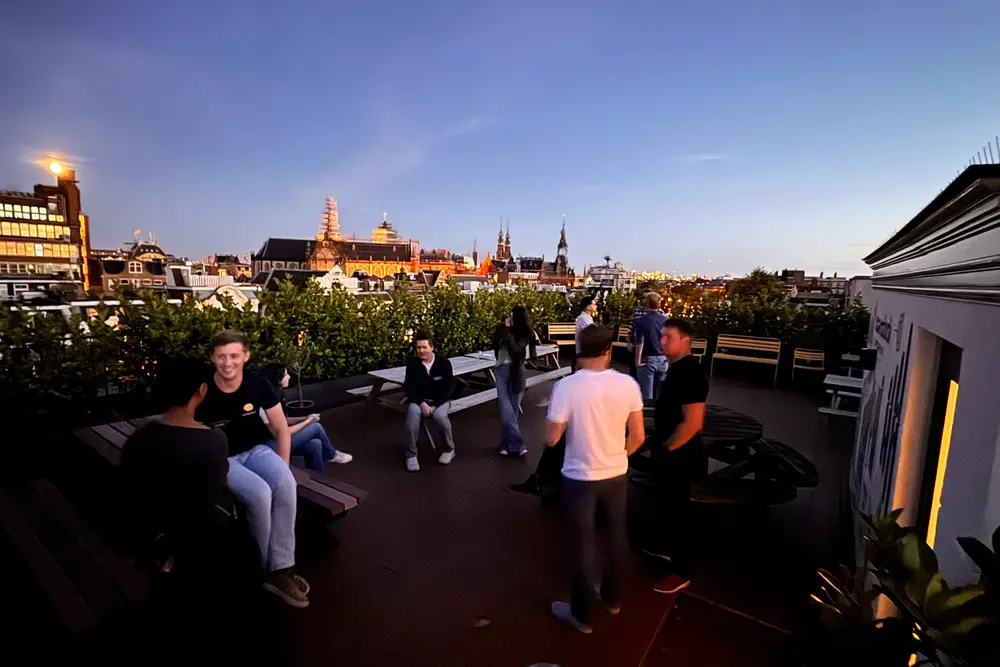 People talking on the rooftop at dusk later that evening, with Amsterdam church towers on the skyline behind them.
