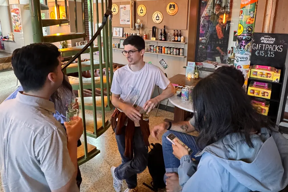 A small group talking with drinks by the green spiral staircase, one of them sitting on a stool and smiling.